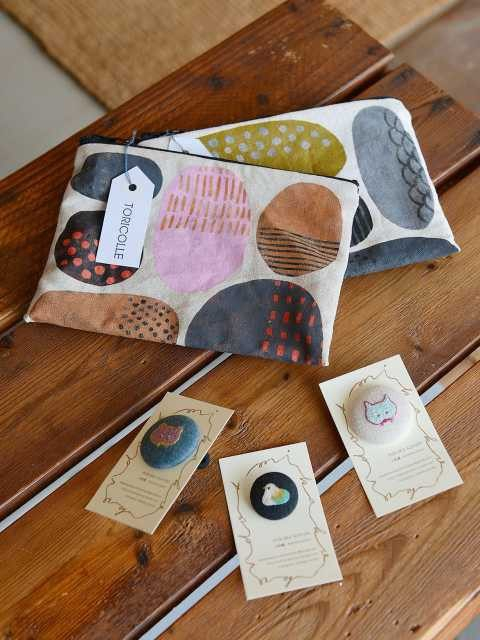 ハンドプリントのポーチ(上)各2700円 刺繍ブローチ(下)各2000円〜